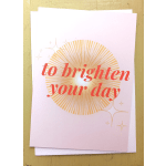 Folded pastel card with coral text 'to brighten your day' over a golden sunburst and small star accents.