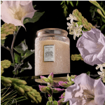 A scented candle in a glass jar surrounded by pale flowers