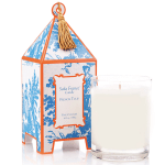 White candle in a glass tumbler beside a patterned box with tassel