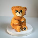 Orange plush teddy bear sitting on a white pedestal