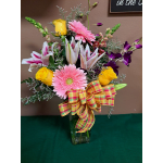 Mixed bouquet of pink gerbera daisies, yellow roses, lilies, and orchids in a glass vase