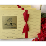 Stacked gold Godiva chocolate gift boxes with red ribbon beside red flowers