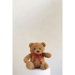 Brown teddy bear with a red ribbon sitting on a white pedestal