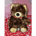 Brown teddy bear with a red ribbon sitting on red patterned fabric