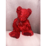 Red plush teddy bear with a ribbon bow sitting on a light surface