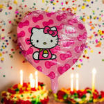 Pink Hello Kitty birthday balloon with confetti and lit cakes in the background