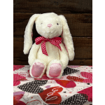 White plush bunny with a pink polka-dot bow sitting on a heart-patterned quilt