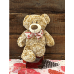 Plush teddy bear with a heart-patterned bow sitting on a red glass vase
