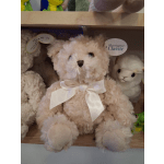 Plush teddy bear with a white ribbon bow sitting on a shelf