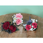 Three small rose corsages with baby's breath on a wooden surface