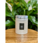 White scented candle in a patterned glass jar on a wooden table