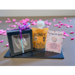 Gift set with honey, a small boxed item, and a card on a tray with pink petals