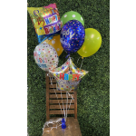 Birthday balloons tied to a wooden chair against a green hedge wall