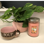 Potted green houseplant beside a pink candle and a soup mug