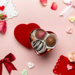 Heart-shaped box of assorted chocolates on a pink background with Valentine decorations