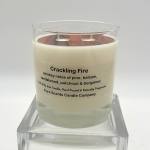Cream-colored soy candle in a clear glass jar labeled Crackling Fire on a clear stand