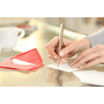 Hands writing on a white card beside red envelopes on a table