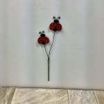 Metal pick with two red and black ladybug decorations on slender black stems