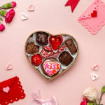 Heart-shaped box of assorted chocolates on a pink background with Valentine decorations