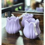 Three lavender tulip-shaped candles on a dark wooden surface
