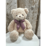 Cream teddy bear with a plaid bow sitting on a white surface