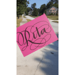 A pink sign with the name "Rita" held outdoors on a suburban street.