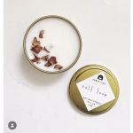 Two gold tin candles on a white surface, one open with dried petals