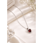 Silver heart pendant necklace with a red gemstone on satin fabric