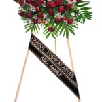 Standing spray of red roses and carnations with white filler flowers on an easel with a black ribbon.