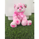 Pink teddy bear with a satin bow sitting on grass