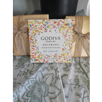 Godiva Goldmark assorted chocolate box with confetti design between gold wrapped gifts with bows
