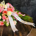 Pink and white floral spray with white ribbon reading 'Mom & Grandma' on a dark wood table