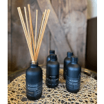 Set of matte black NOMAD reed diffuser bottles with wooden sticks on a woven mat