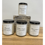 Four scented candles in glass jars with black lids on a wooden surface
