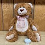Brown teddy bear with a pink plaid ribbon sitting beside a tealight candle