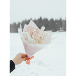 Handheld bouquet of small white flowers and dried accents wrapped in pink paper with a ribbon in a snowy field