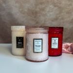 Trio of embossed glass jar candles in cream, blush pink, and red on a light surface