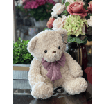 Plush teddy bear with a gingham bow in front of a floral arrangement