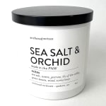 White candle jar with black lid labeled Sea Salt & Orchid
