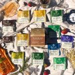 Assorted Piper & Leaf tea packets arranged on a cloth with fruit and a clock