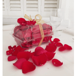 Clear gift box filled with red rose petals and tied with a gold ribbon