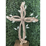 Decorative wooden cross with vine and leaf accents against a green hedge