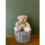 Plush teddy bear sitting in a woven basket with a ribbon bow