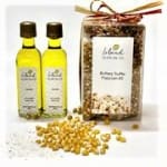 Gourmet popcorn kit with two small bottles of oil, a bag of popcorn mix, and loose kernels on a white background