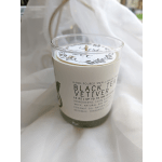 Glass jar candle labeled Black Tea Vetiver on white fabric