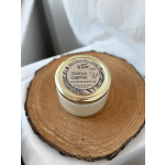 A small candle jar with a gold lid sits on a wood slice.