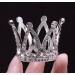 Small silver rhinestone crown held between fingers on a black background