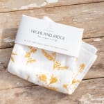 Folded white floral-print cloth with a product tag on a wooden surface