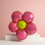 Pink flower-shaped foil balloon with a yellow center on a white pedestal
