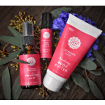 A body mist, roll-on perfume, and body butter arranged with purple flowers